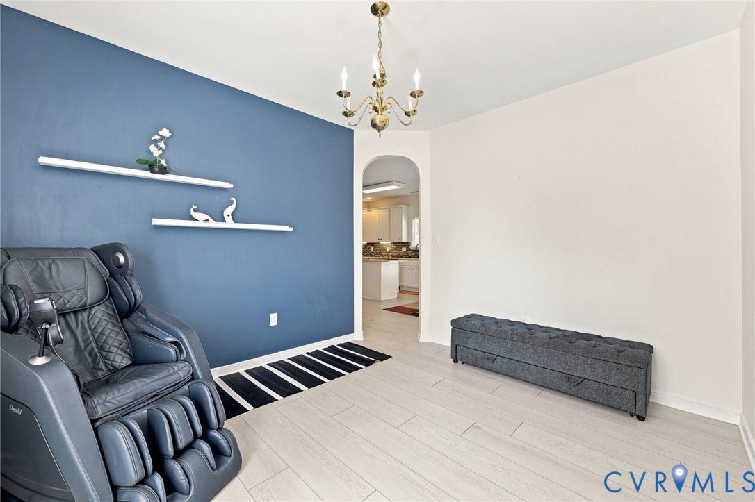 Light wood-finish flooring, a decorative wall with floating shelves, an arched doorway, and a brass chandelier