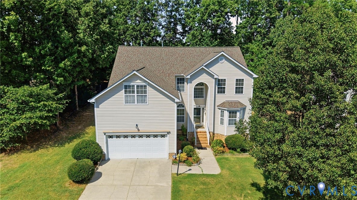 Traditional two-story residence with light-colored siding, an attached two-car garage, mature trees, and a concrete driveway