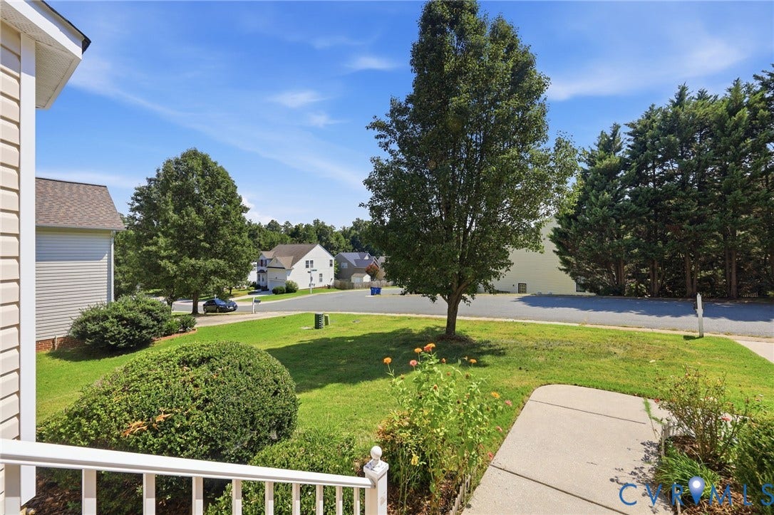 Manicured front yard with mature trees, established shrubs, and a concrete walkway