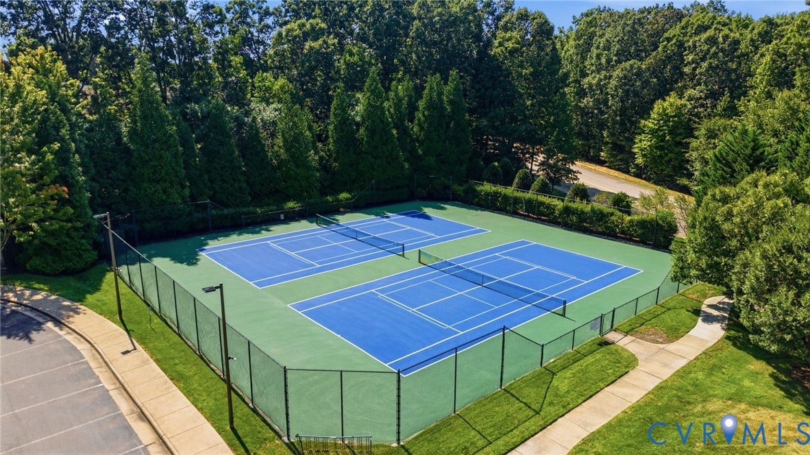 Two tennis courts with blue playing surfaces and green surrounds, enclosed by dark fencing