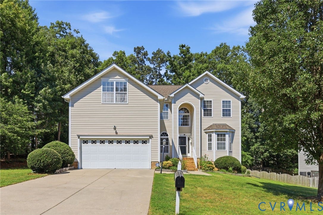 Two-story exterior with light-colored siding, a two-car garage, established landscaping, and a concrete driveway