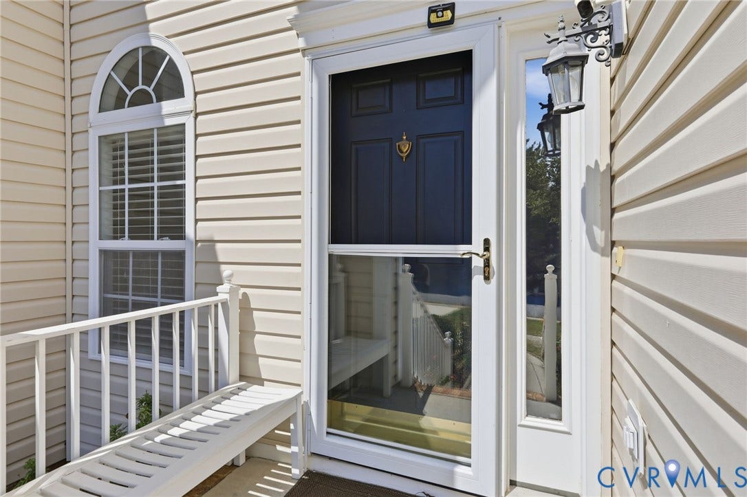 Cream-colored vinyl siding exterior with a dark-paneled front door, an arched transom window, a white storm door, and an ornate wall-mounted lantern