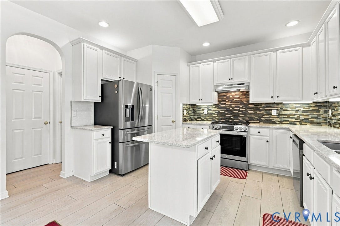 Kitchen featuring white cabinetry, light-toned countertops, a mosaic tile backsplash, stainless steel appliances, and wood-finish flooring