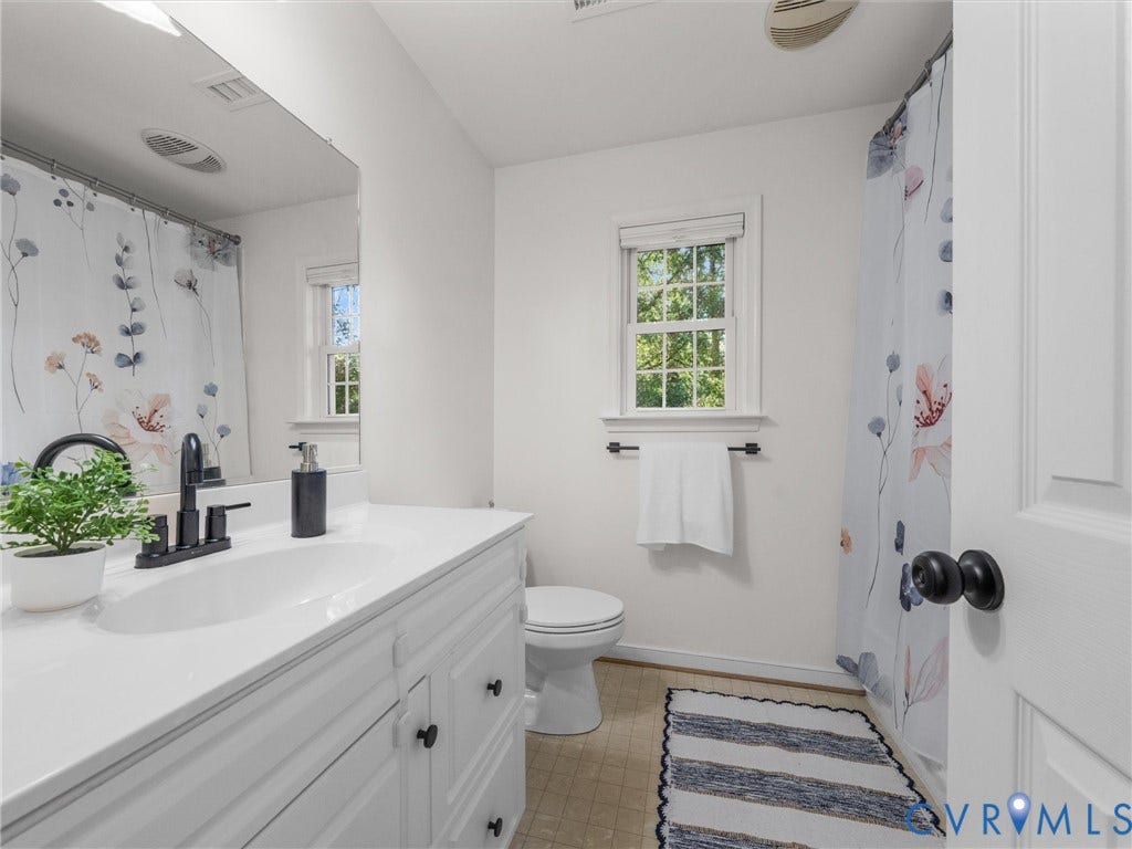 White vanity with integrated sink, black matte faucet, framed mirror, and window with natural light