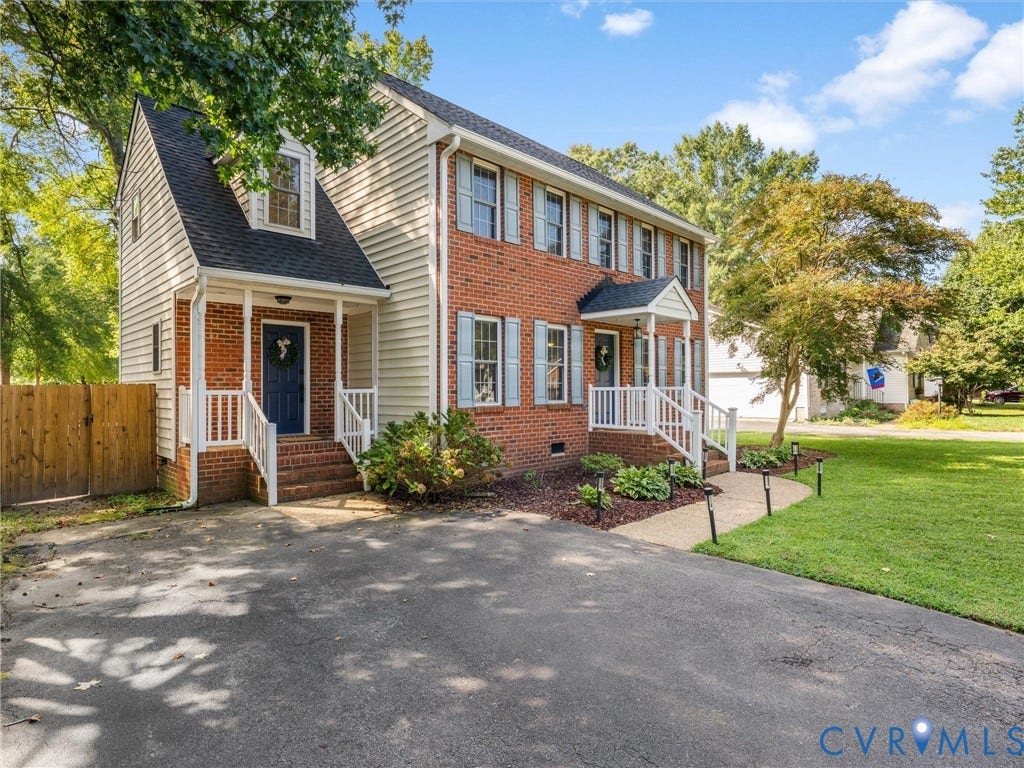 Brick and siding exterior with dual front porches, a paved driveway, a landscaped front yard with decorative lighting, and mature trees