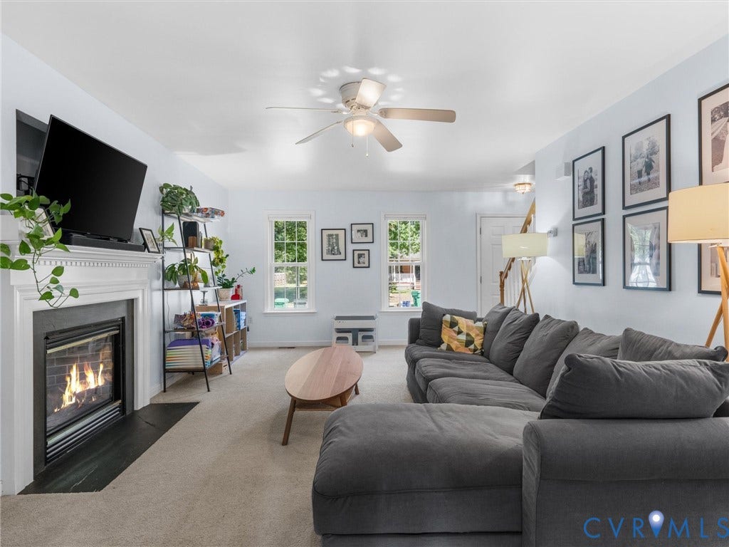 Living area with a built-in fireplace featuring a white mantel, ceiling fan, and multiple windows