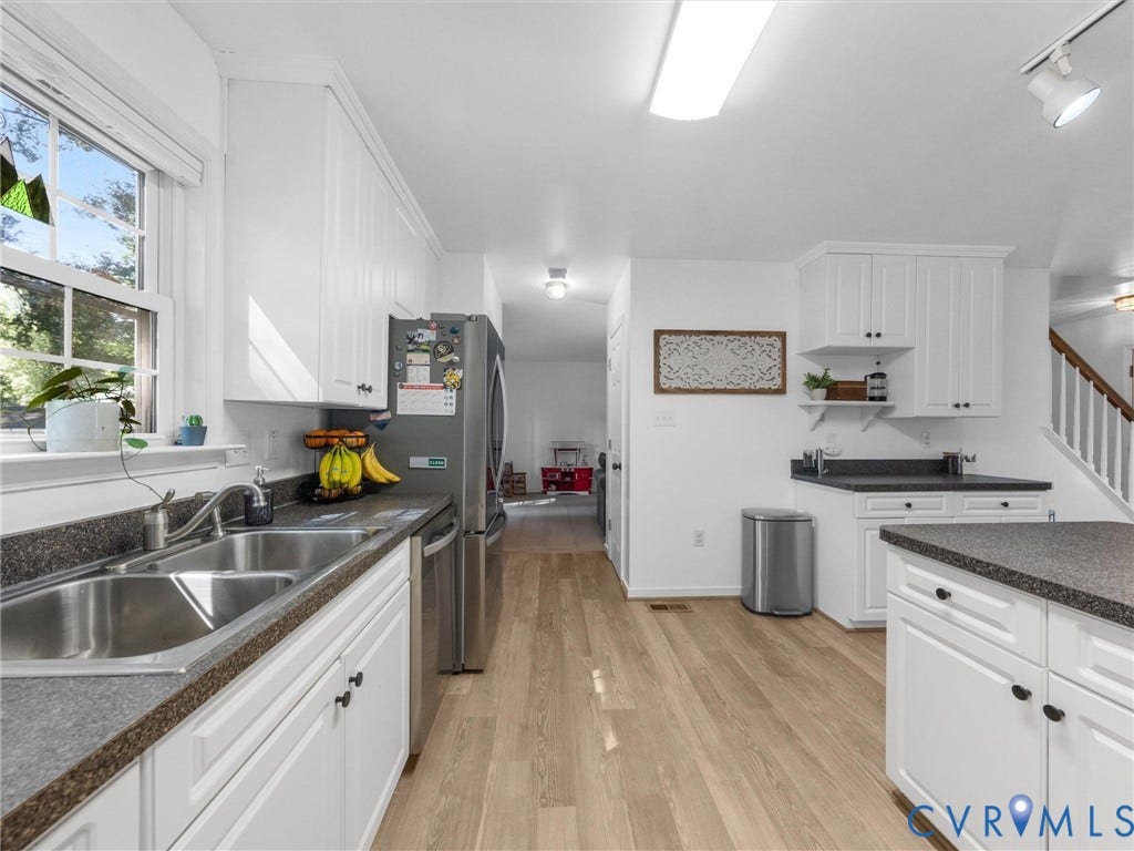 Contemporary kitchen featuring white cabinetry, dark countertops, a stainless steel double basin sink, stainless steel appliances, and wood-finish flooring