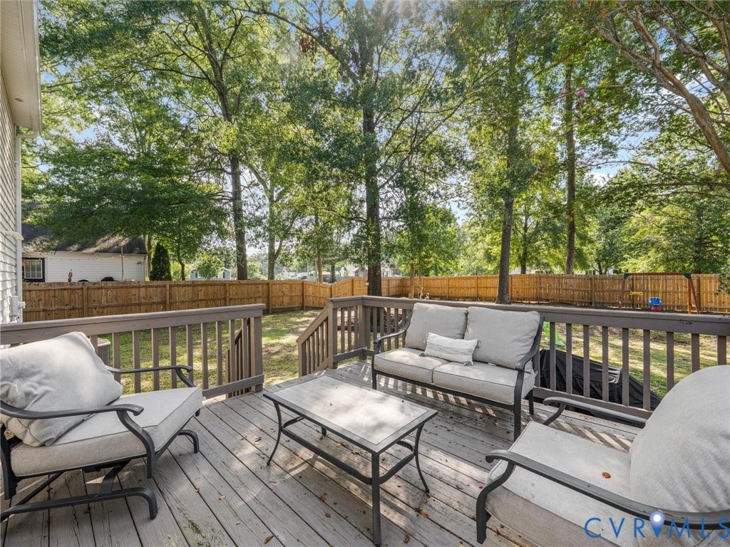 Expansive wood deck with a full railing system, surrounded by mature trees and a wood privacy fence