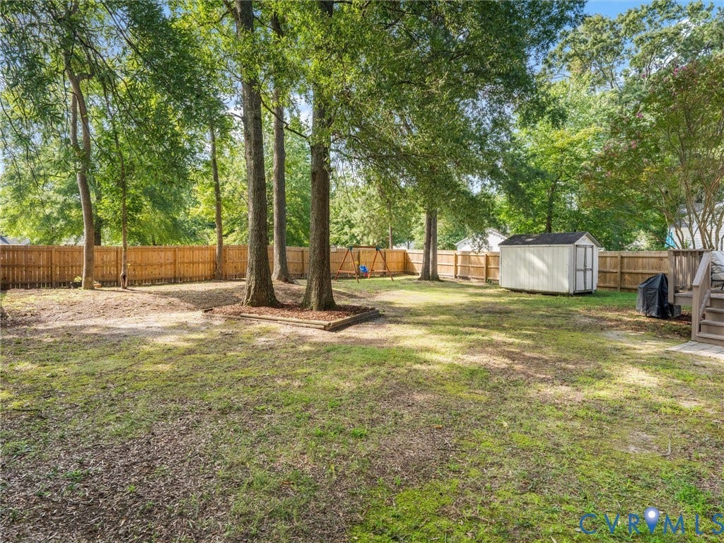 Expansive backyard featuring mature trees, a wood privacy fence, a storage shed, and a wood deck with stairs