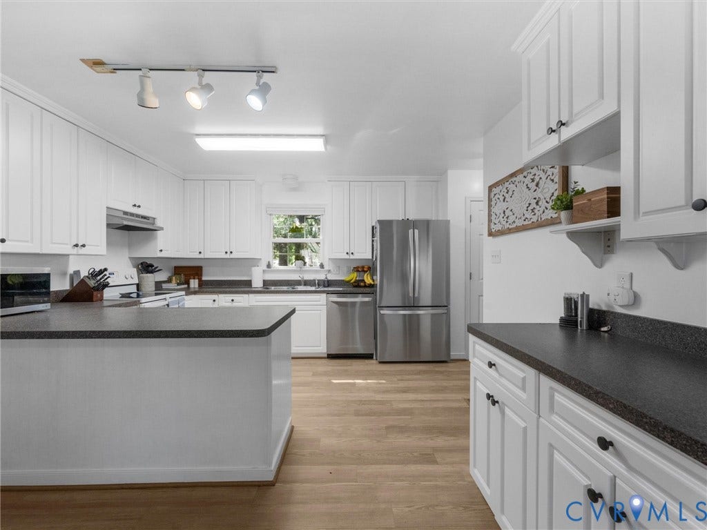 White cabinetry with black hardware, stainless steel appliances, dark countertops, wood-finish flooring, and a track lighting fixture