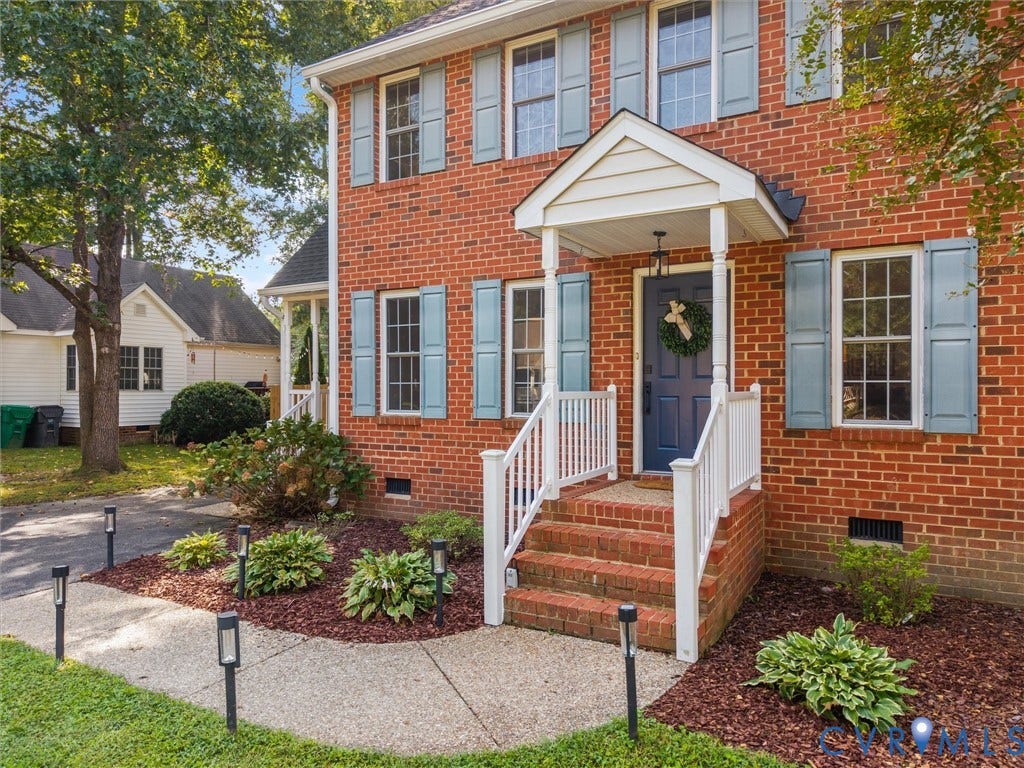 Brick exterior with light blue window shutters, concrete walkway, porch with white railings, and brick steps