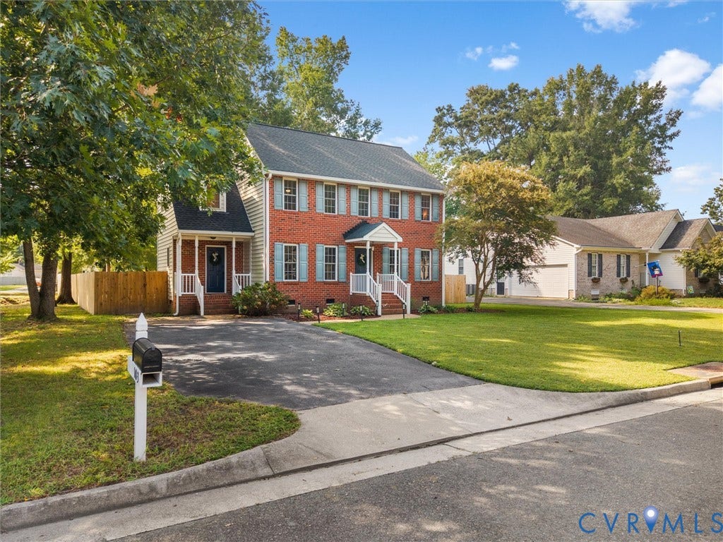 Brick exterior with light blue shutters, dual entry porches with white railings, mature trees, and a paved driveway