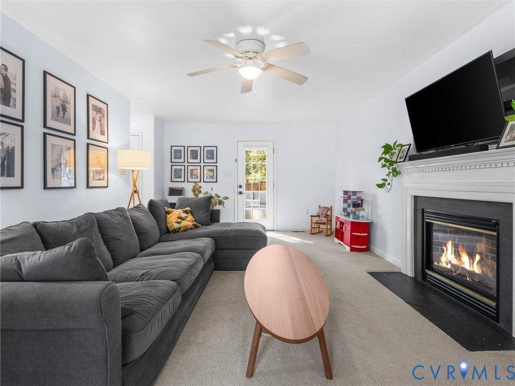 Carpeted living area featuring a ceiling fan, a fireplace with a white mantel, and a glass-paned door