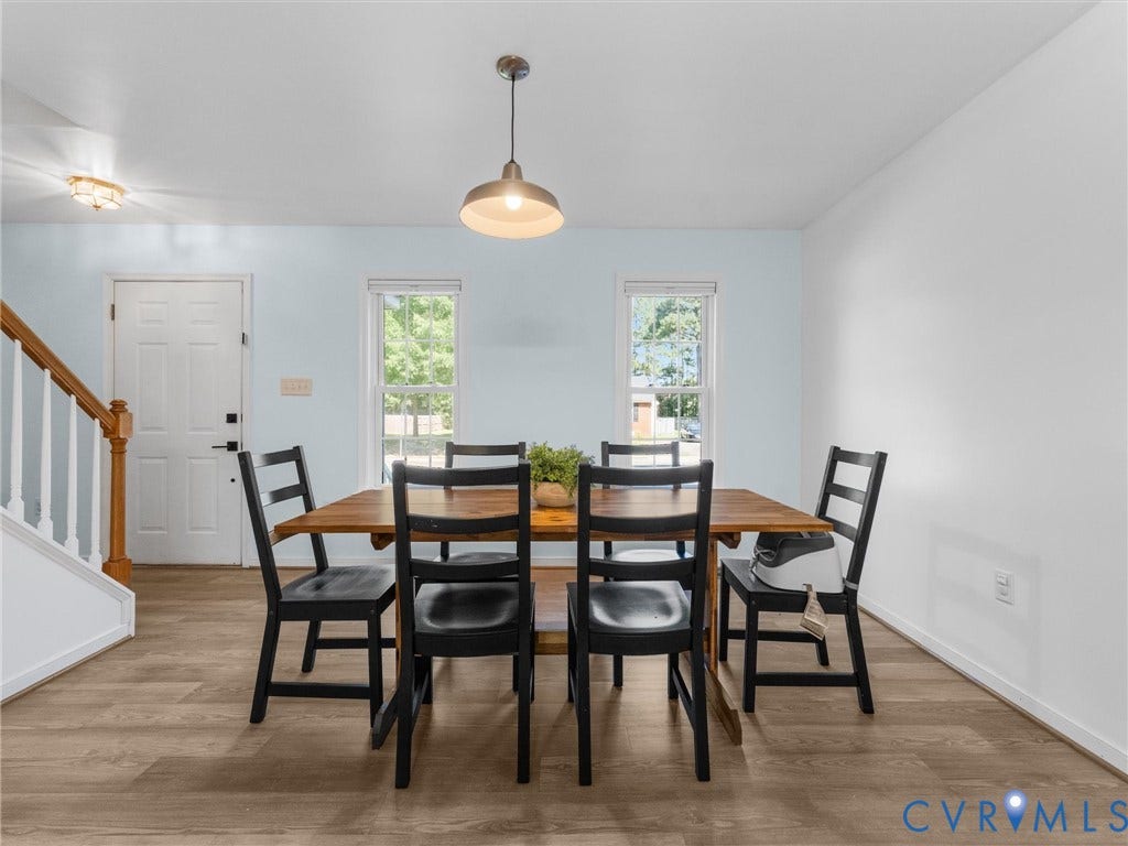 Wood-finish flooring, white paneled door, two windows, suspended pendant lighting, and a wood handrail with white balusters