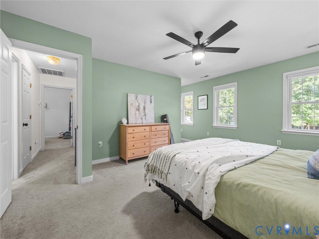 Soft green walls with multiple windows, a ceiling fan with integrated lighting, and neutral-toned carpeting
