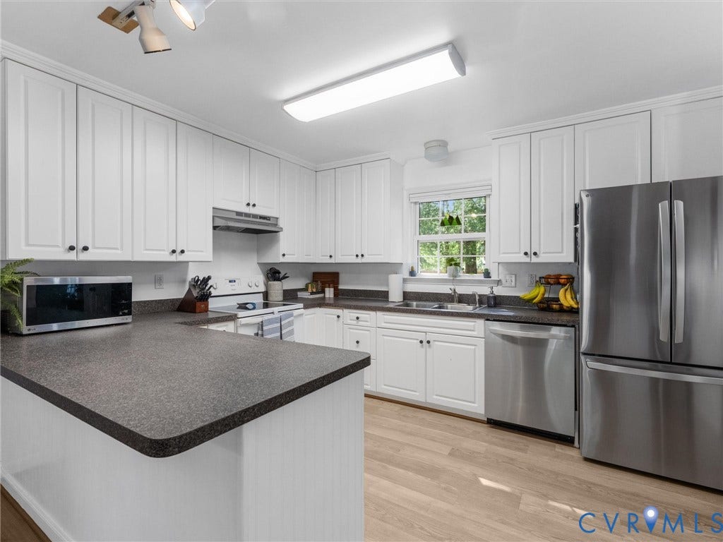 White cabinetry with dark hardware, stainless steel appliances, dark speckled countertops, wood-finish flooring, and a window above the sink