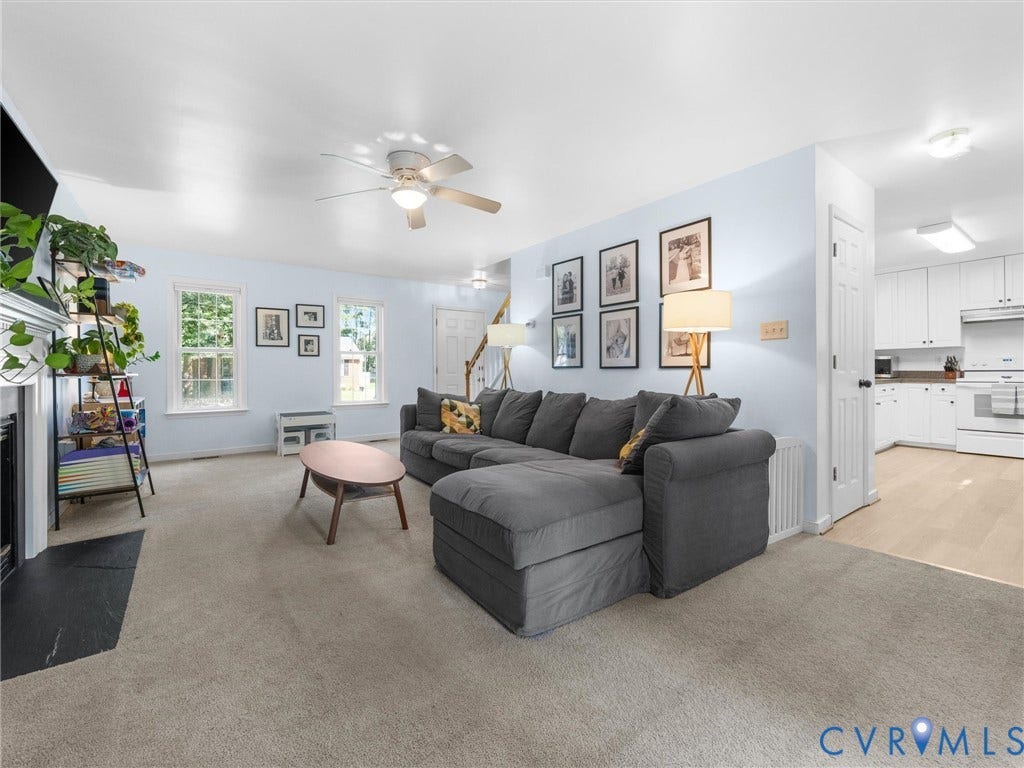 Carpeted living space with a ceiling fan, fireplace, and multiple windows