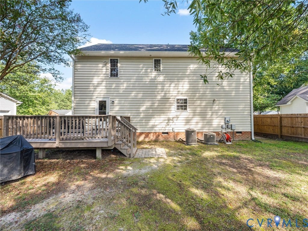 Spacious rear yard featuring a wooden deck with railing, a privacy fence, and mature trees