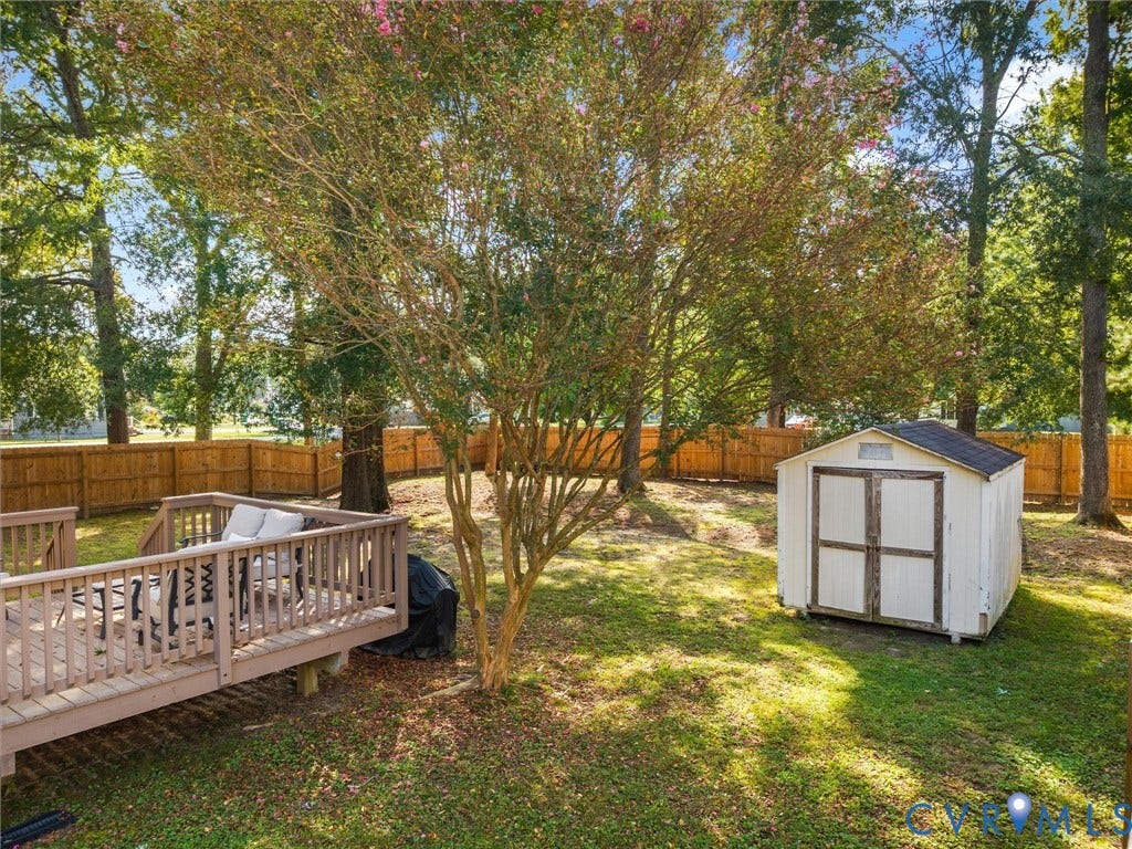 Expansive backyard featuring a wood deck, storage shed, mature trees, and privacy fencing
