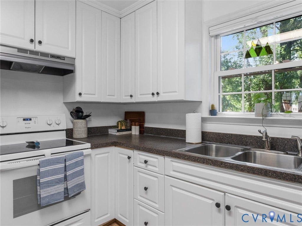 White cabinetry with black hardware, double basin stainless steel sink, dark speckled countertops, smooth-top electric range, and a window with natural light