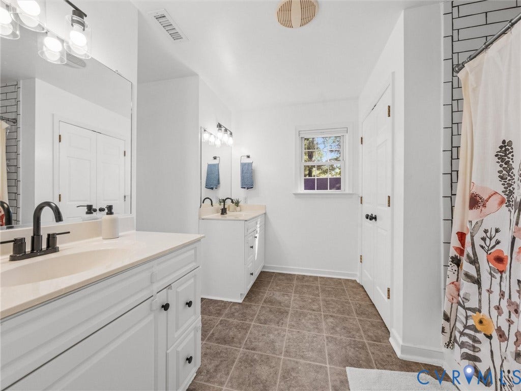 Dual white vanity cabinets with integrated sinks, matte black fixtures, tile flooring, and a single window