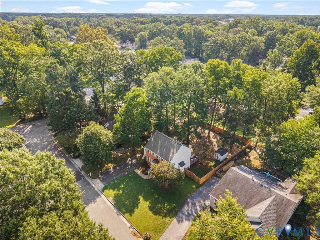 Corner lot property featuring a paved driveway, mature trees, a fenced backyard, and an exterior storage shed