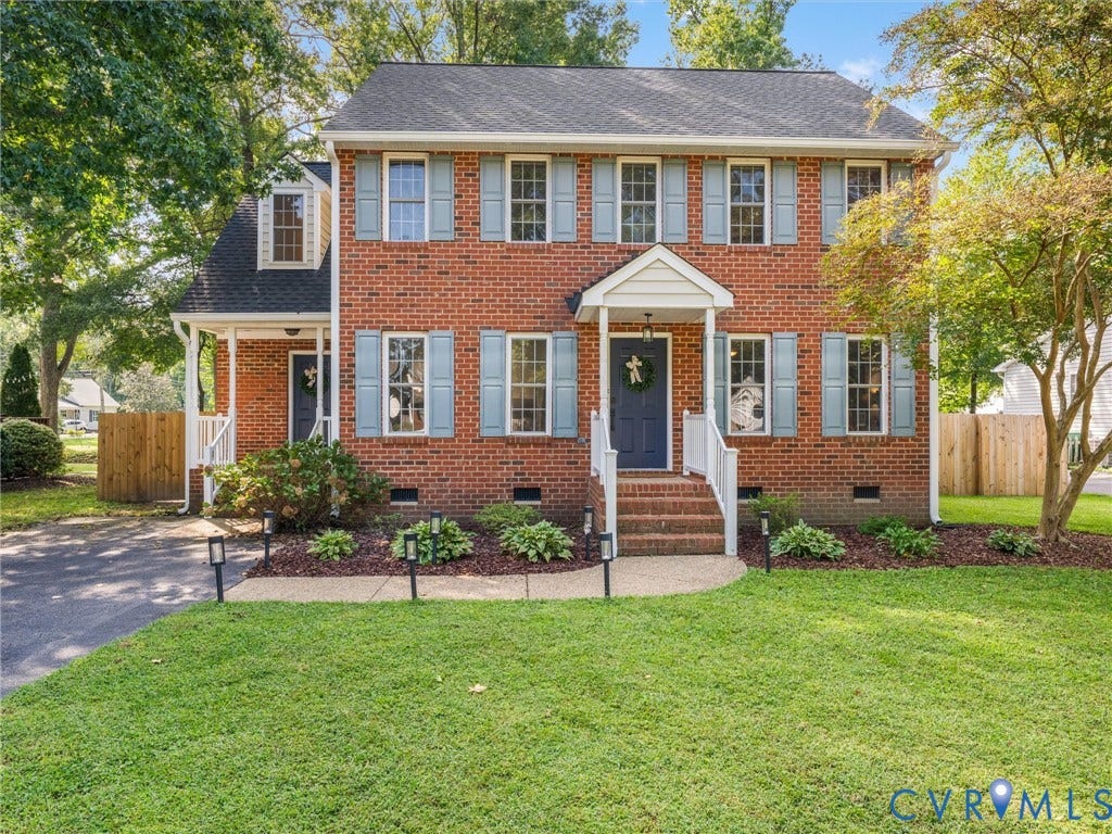 Brick facade with light blue shutters, a covered front entry, established landscaping, and a manicured lawn