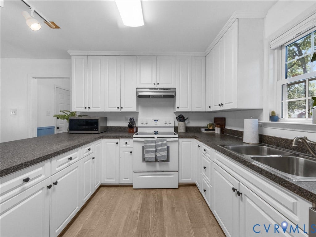 White shaker-style cabinetry with dark hardware, a double basin stainless steel sink, wood-finish flooring, a built-in range with an overhead vent, and ample counter space