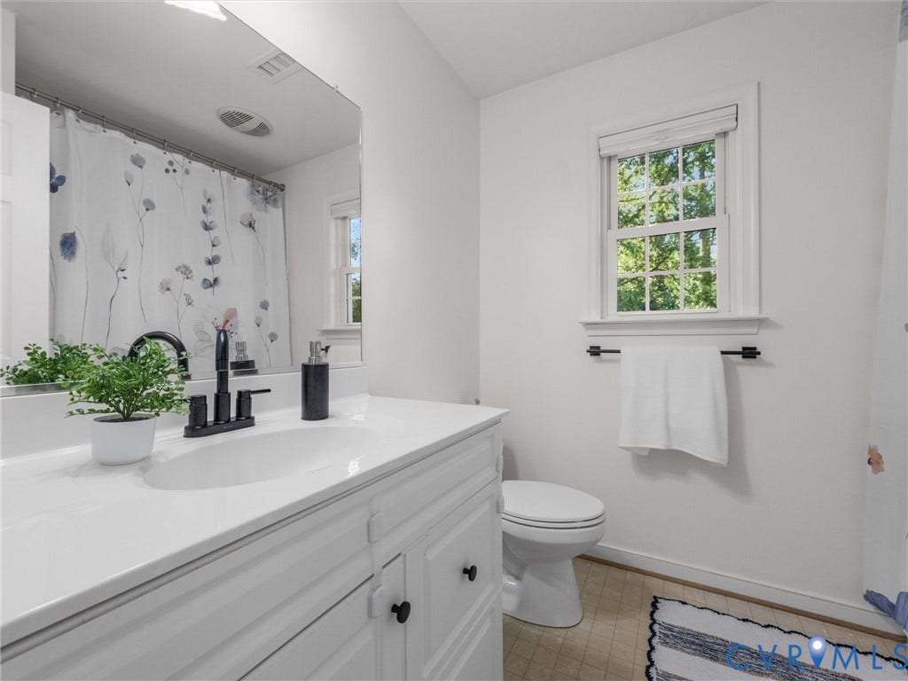 White vanity with integrated sink and matte black faucet, wall-mounted mirror, white toilet, and window with natural light