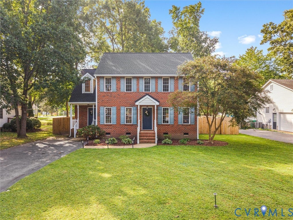 Red brick exterior with dark shutters, gabled dormer, and mature trees