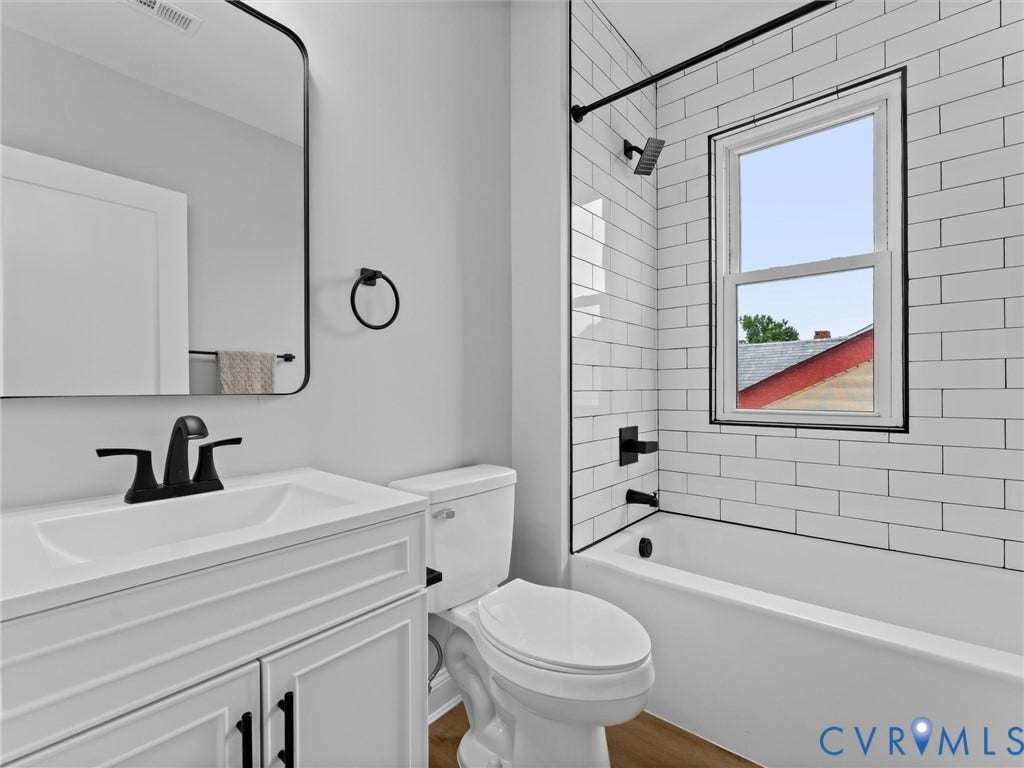 2623 Northumberland Avenue, Richmond, VA 23220 Contemporary bathroom featuring a white vanity with integrated sink, matte black fixtures, a rectangular mirror, subway tile shower surround, and a window within the shower area