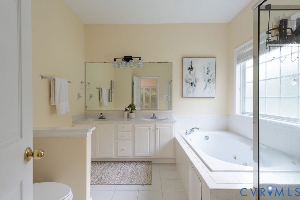 14107 Beachmere Road, Stoney Glen South, Chester, VA 23831 Dual vanity with integrated sinks, built-in soaking tub, glass-enclosed shower, transom window, and white tile flooring