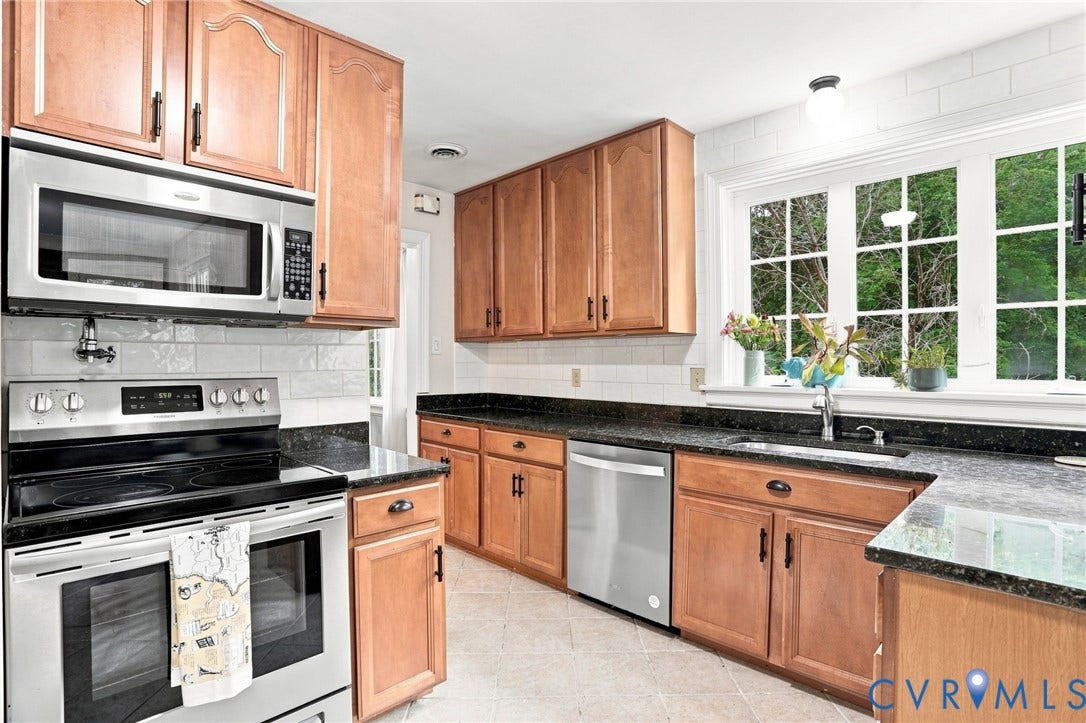 1427 Spring Grove Drive, Richmond, VA 23225 Light wood-finish cabinetry with dark hardware, stainless steel appliances, dark stone-finish countertops, white subway tile backsplash, and a large multi-pane window