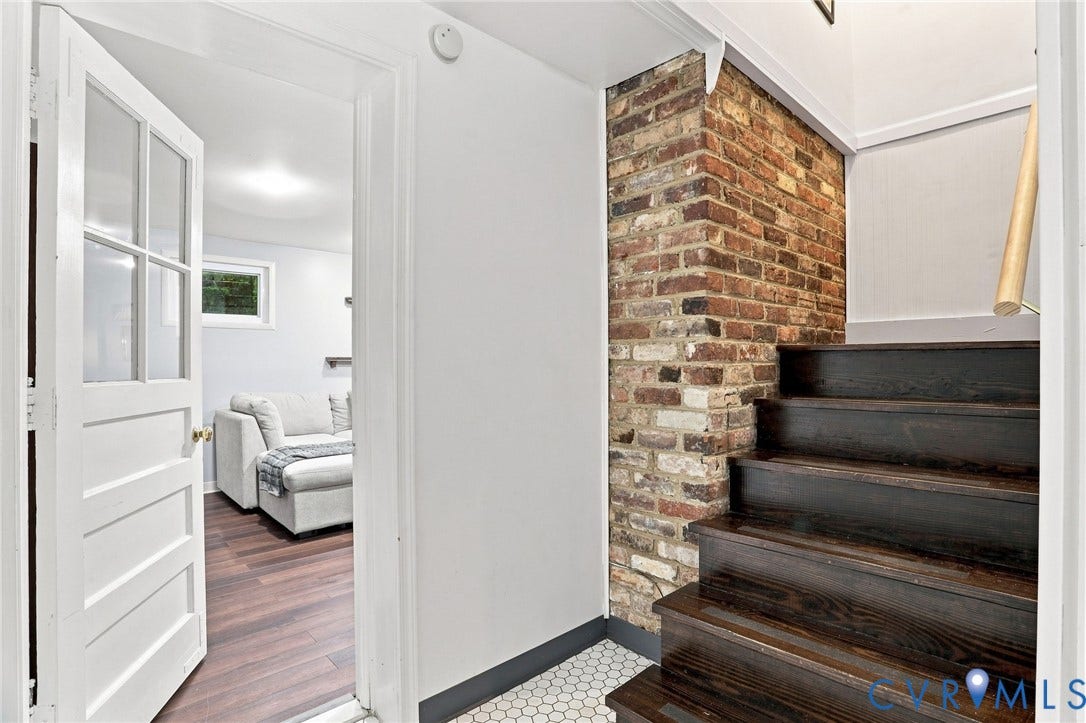 1427 Spring Grove Drive, Richmond, VA 23225 Exposed brick accent wall with dark wood stairs, white hexagon tile flooring, and a white paneled door with glass inserts