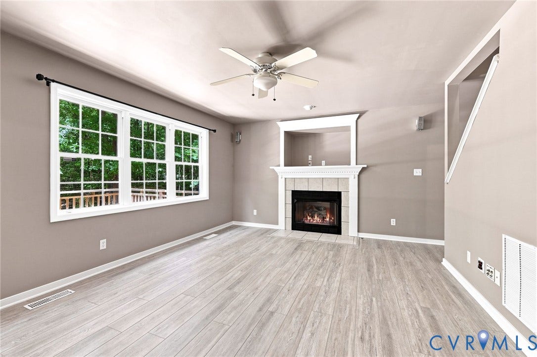 3522 Fairfield Road, Powhatan, VA 23139 Living area featuring light wood-finish flooring, a ceiling fan with integrated lighting, a fireplace with a white mantel and tile surround, and a triple window with white sashes