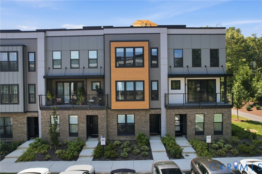 Contemporary townhome row featuring mixed-material facades with warm wood-tone and charcoal gray cladding, large multi-pane windows, and stone base elements