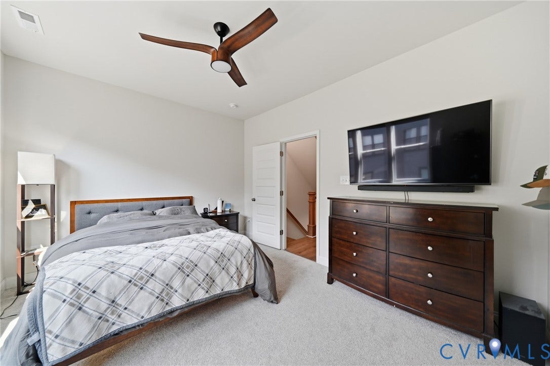 Sloped ceiling with recessed lighting, ceiling fan with wood-finish blades, light-colored carpeting, white interior door, and a built-in wall-mounted television