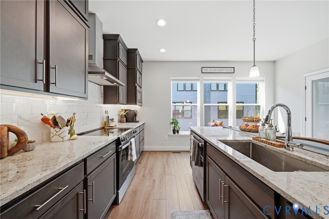 Spacious kitchen featuring dark wood cabinetry, light-toned countertops, a stainless steel sink with a high-arc faucet, and wood-finish flooring