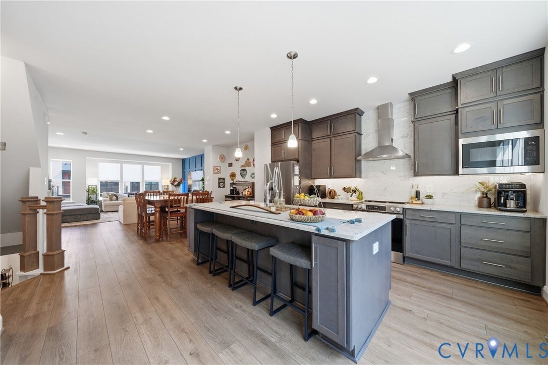 Open-concept living area featuring wood-finish flooring, recessed lighting, and a kitchen with gray cabinetry, stainless steel appliances, and a central island with countertop seating