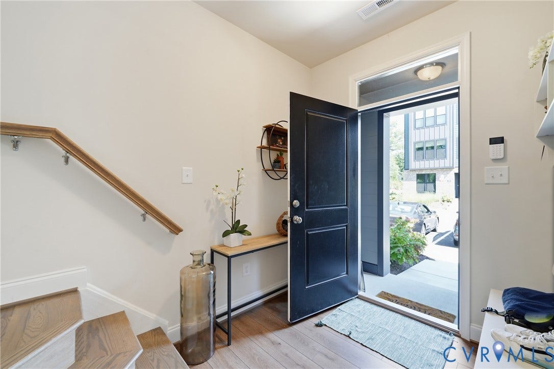 Solid core entry door, wood-finish flooring, staircase with wood handrail, built-in shelving, and contemporary wall sconce