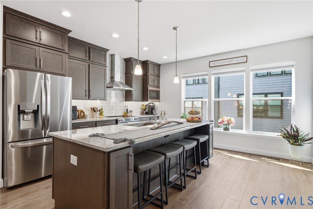 Kitchen featuring wood-finish flooring, dark wood cabinetry, stainless steel appliances, and a large center island with counter seating