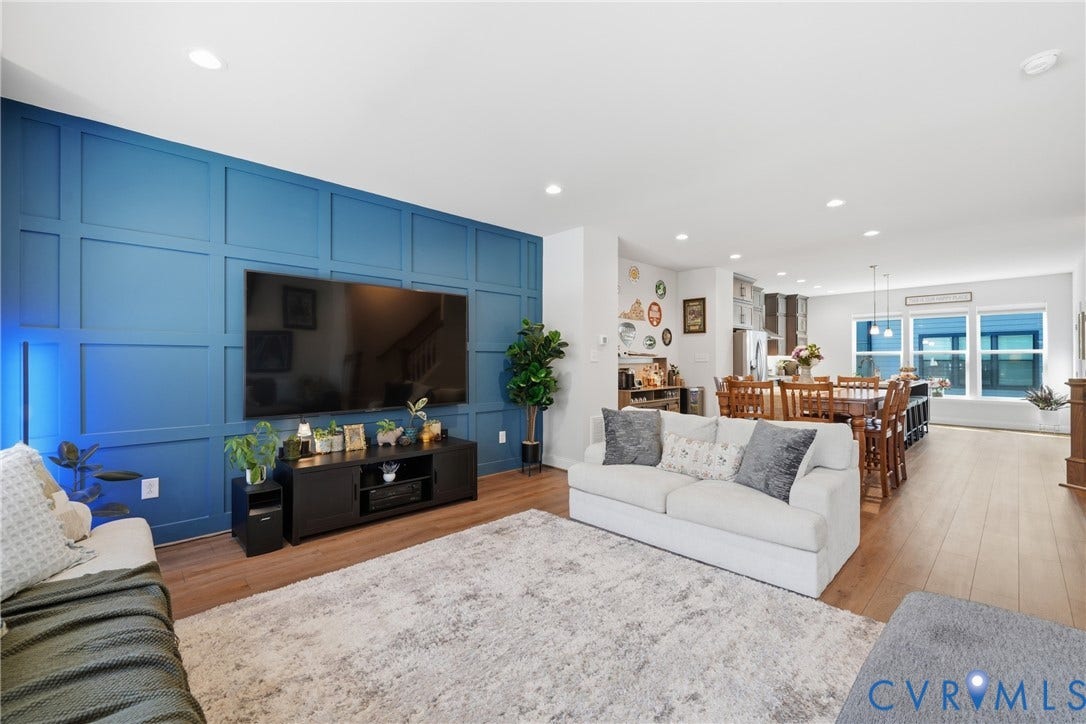 Open-concept living area featuring a decorative accent wall, wood-finish flooring, recessed lighting, and a kitchen with an island