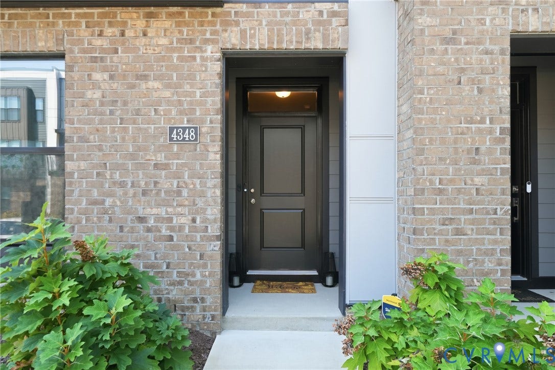 Brick exterior facade with a dark paneled entry door, transom window, and concrete entry path