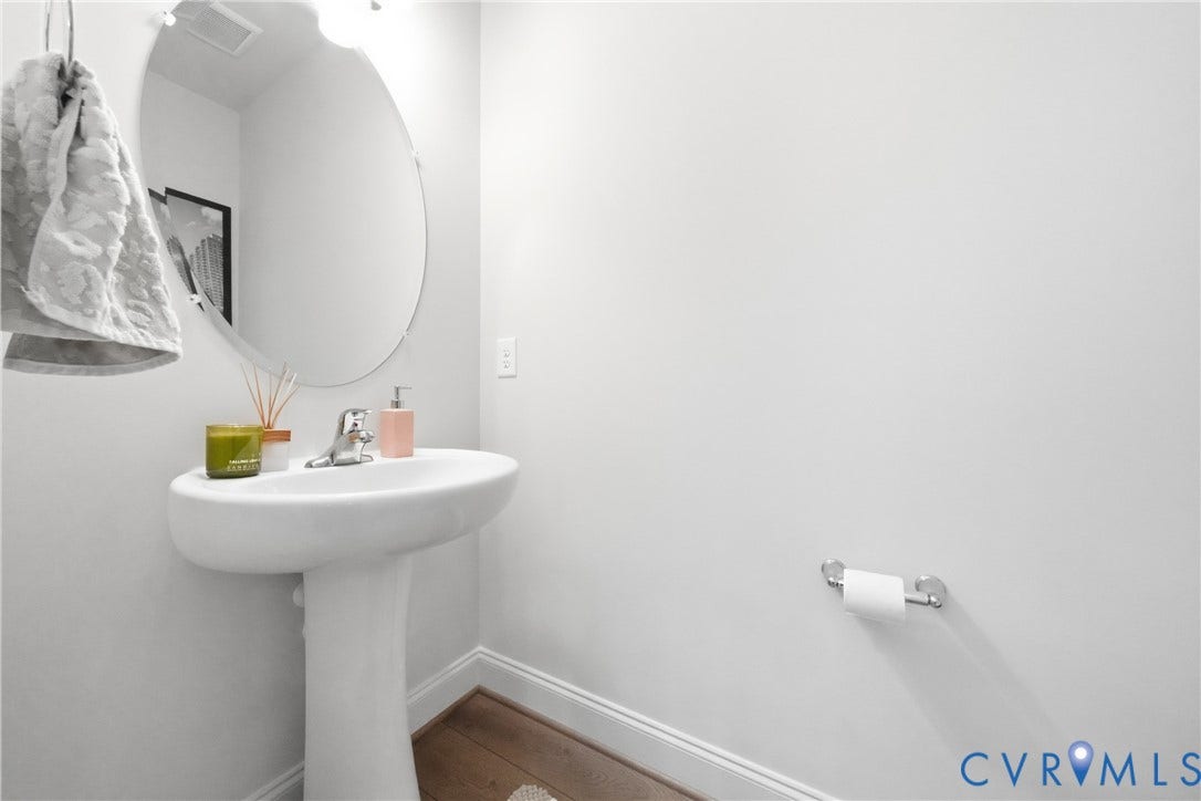 Pedestal sink with chrome faucet, oval mirror, and wood-finish flooring