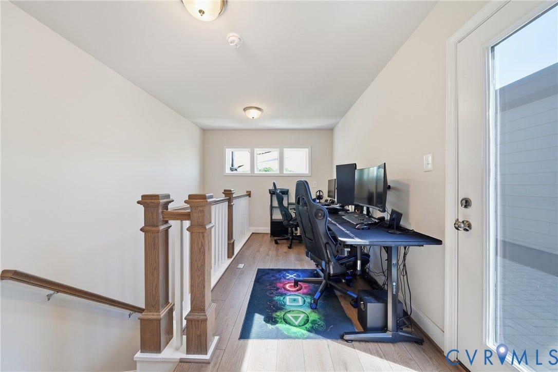 Hallway with wood-finish flooring, white walls, and a wood-finish staircase railing