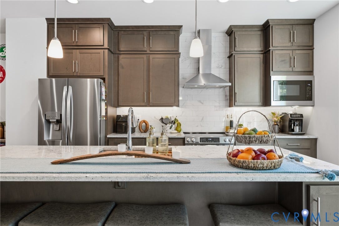 Stainless steel appliances, built-in microwave, wood-finish cabinetry, subway tile backsplash, and a large island with sink