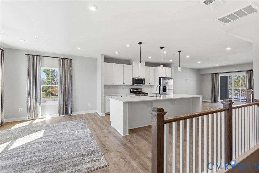 Open-concept living area featuring wood-finish flooring, recessed lighting, and a kitchen with white cabinetry