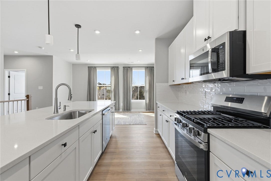 Kitchen featuring white cabinetry, stainless steel appliances, a large island with an undermount sink, and light wood-finish flooring