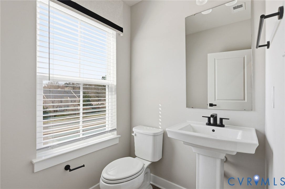 Pedestal sink with a matte black faucet, wall-mounted mirror, and white window blinds