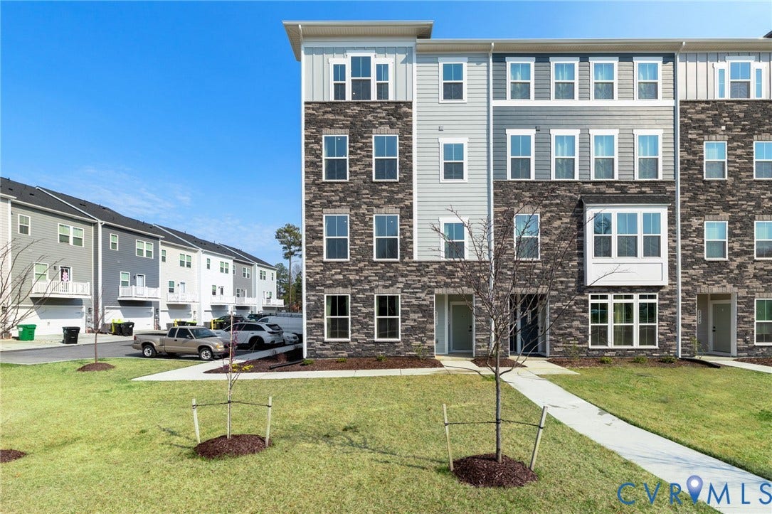 Multi-story townhouse featuring a stone and siding exterior, multiple windows, and a paved walkway